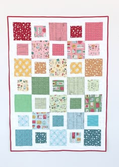 a patchwork quilt hanging on the wall in front of a white wall with red trim