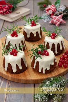 small cakes with white icing and cherries on a wooden platter next to greenery