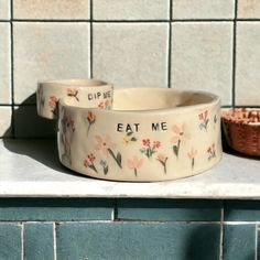 two dog bowls with words on them sitting on a counter top next to a bowl that says eat me