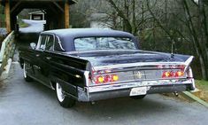 an old black car parked in front of a covered bridge