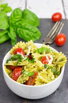 a white bowl filled with pasta, tomatoes and spinach on top of a table