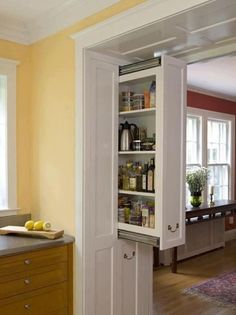 an open cabinet in the middle of a kitchen with yellow walls and white trim on the doors