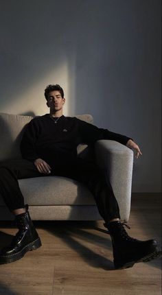 a man sitting on top of a couch next to a white wall and wooden floor