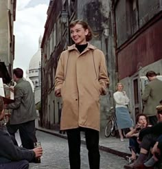 a woman standing in the middle of an alleyway with people sitting on the sidewalk