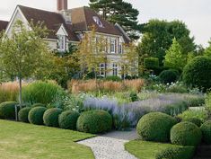 a large house sitting next to a lush green field with lots of trees and bushes