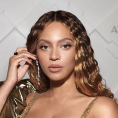 a close up of a person wearing a gold dress and holding a pair of earrings