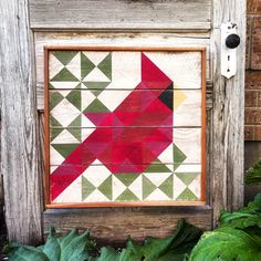 a red bird painted on wooden planks in front of some green leaves and plants