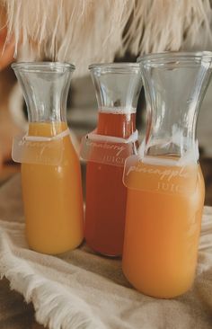 three glass pitchers filled with liquid sitting on top of a table next to each other