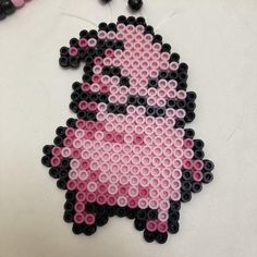 a pink and black beaded sheep ornament on a white table next to beads