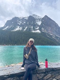 a woman sitting on the edge of a stone wall next to a lake