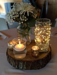 some candles are sitting on a table with flowers in the vase and lights around it