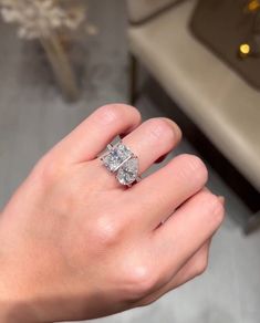 a woman's hand with a diamond ring on top of her finger, in front of a couch