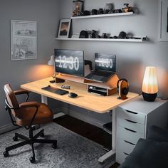 a desk with two computer monitors on top of it next to a chair and lamp