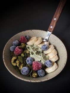 a bowl filled with fruits and vegetables on top of a black table next to a spoon