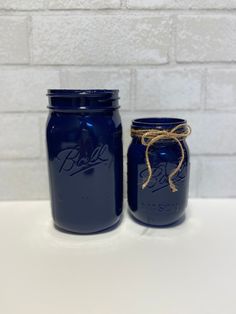 two blue mason jars with rope tied around the lids on a white countertop next to a brick wall