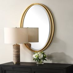 a table with a lamp, mirror and vase on it next to a black dresser