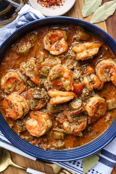 a blue bowl filled with shrimp and tomato stew on top of a wooden cutting board