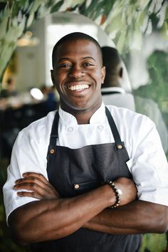 a man wearing an apron and smiling at the camera with his arms crossed in front of him