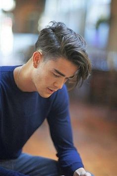 a young man sitting on the floor looking at his cell phone while holding it in his hand