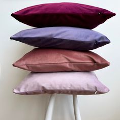 four pillows stacked on top of each other in different colors and sizes, sitting on a white stool