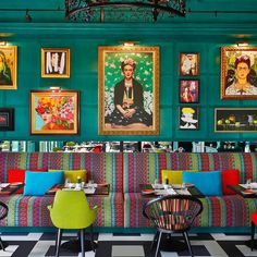 a restaurant with green walls and paintings on the wall, colorful chairs and tables in front of them