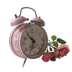 an old fashioned pink alarm clock next to flowers