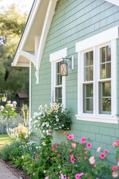 a green house with white windows and flowers in the foreground, along side it