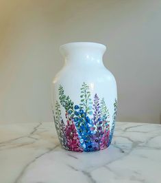 a white vase sitting on top of a marble table covered in colorful flowers and leaves