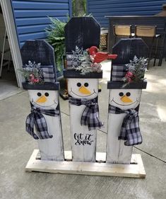 three snowmen with hats and scarfs are sitting in front of a blue house