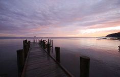 a wooden dock sitting on top of a body of water under a purple cloudy sky