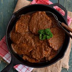 a skillet filled with beef and broccoli on top of a red checkered cloth