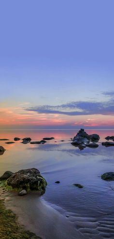 the sun is setting over the water and rocks on the beach in front of it