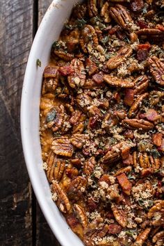 a white dish filled with pecans and other food on top of a wooden table