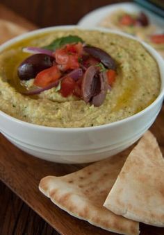 a white bowl filled with hummus and olives