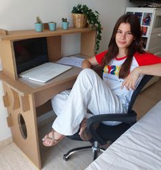 a woman sitting at a desk with a laptop computer on top of it and her legs crossed