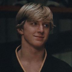 a young man with blonde hair wearing a black shirt and gold collared necktie