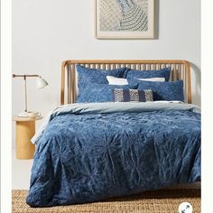 a bed with blue comforters and pillows in a white room next to a painting on the wall