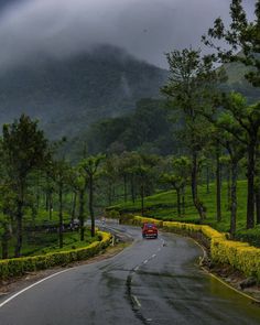 a red car driving down a road next to lush green trees and mountains in the background