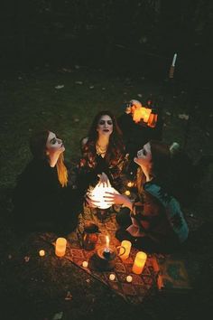 three women sitting on the ground with candles in their hands