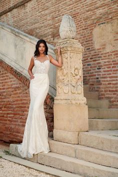 a woman in a wedding dress leaning against a stone pillar on the steps next to an old brick building