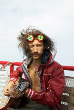 a man sitting on a bench with his hair blowing in the wind and sunglasses over his eyes