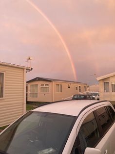 a car parked in front of a house with a rainbow in the sky