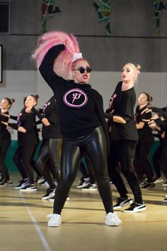 a group of women in black outfits and pink hair are dancing on a dance floor