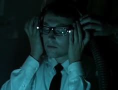 a man wearing glasses and a tie is holding his headphones to his ears in the dark