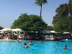 people are swimming in a large pool surrounded by umbrellas and lounge chairs, with trees