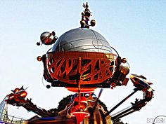 an amusement park ride with metal sculptures and lights on it's sides, against a blue sky