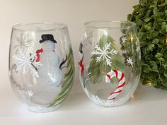 two wine glasses decorated with snowmen and candy canes are sitting next to a potted plant