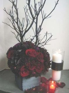 a vase filled with red roses next to a candle and some branches on a table