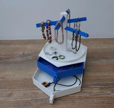 an assortment of jewelry sits on top of a white stand with blue strips holding bracelets and necklaces