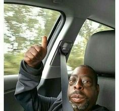 a man sitting in the back seat of a car holding his hand up and smiling